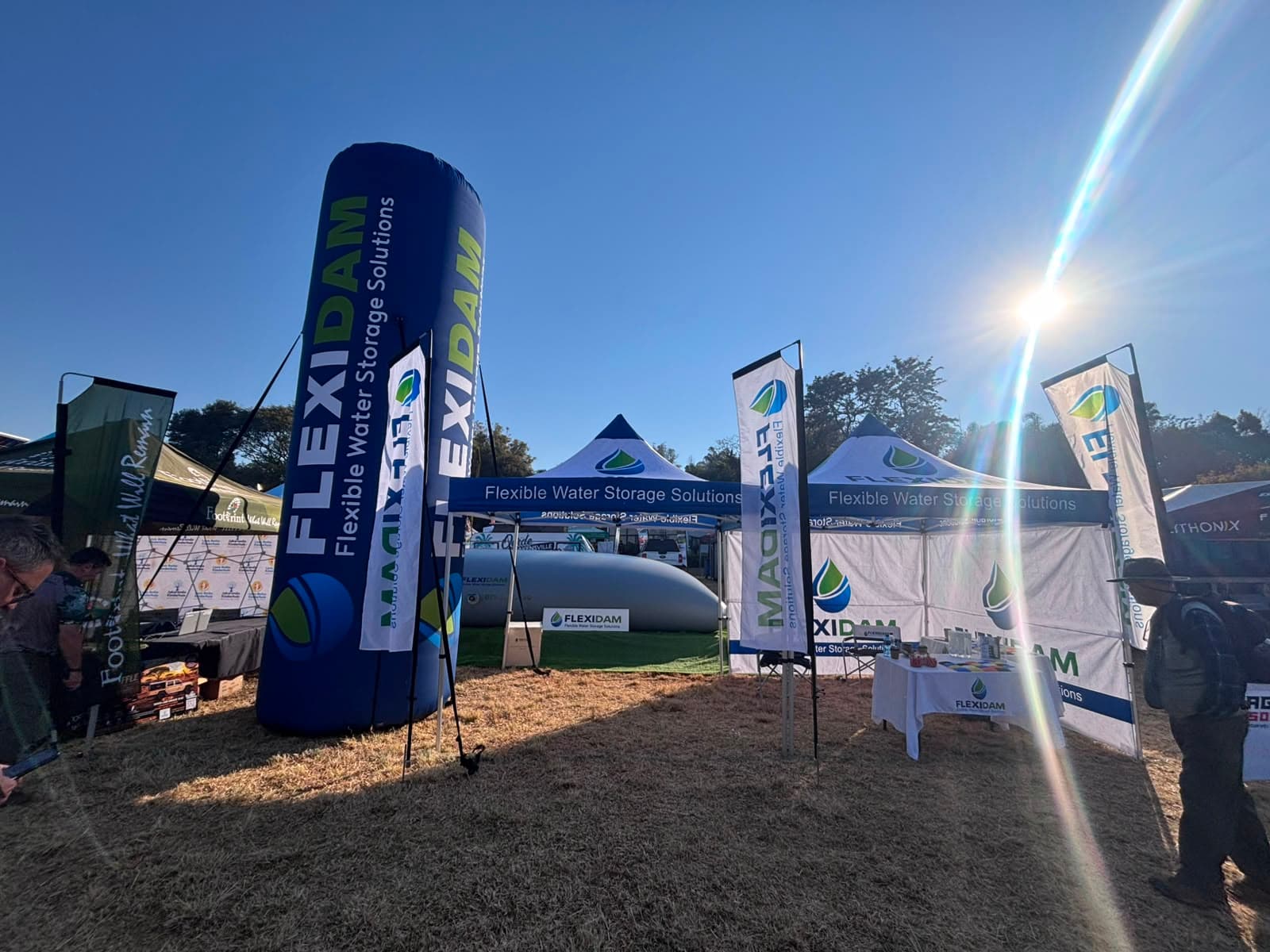 The FlexiDam stand at KragDag 2026: branded gazebos, feather flags and an inflatable FlexiDam pillar around a filled pillow tank
