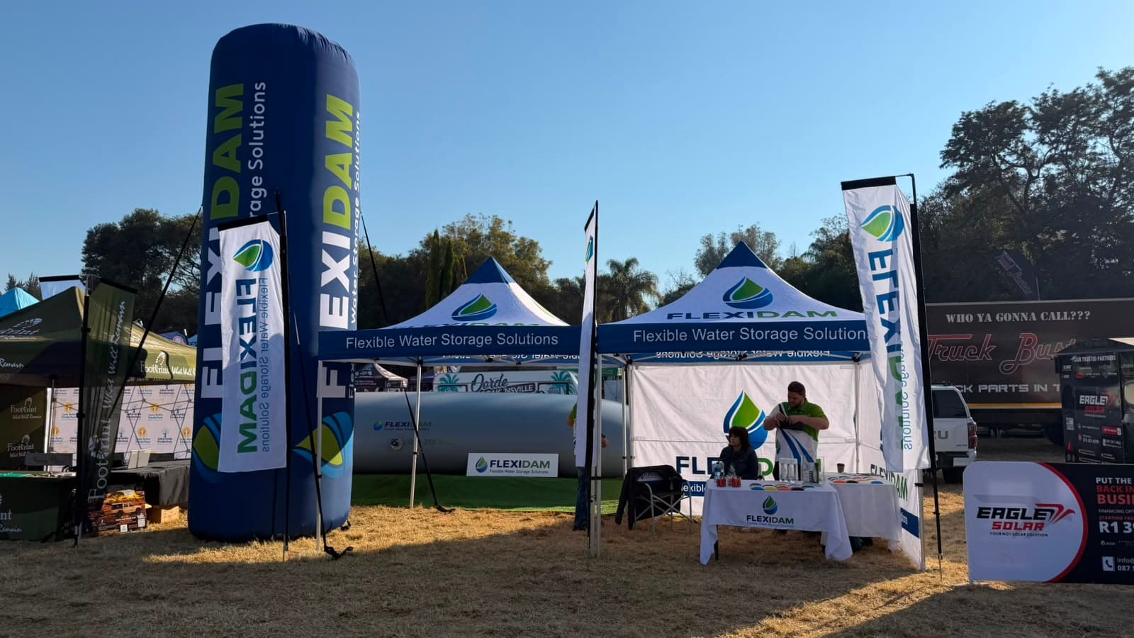 A filled FlexiDam pillow tank on the stand at KragDag 2026, flanked by branded gazebos and feather flags