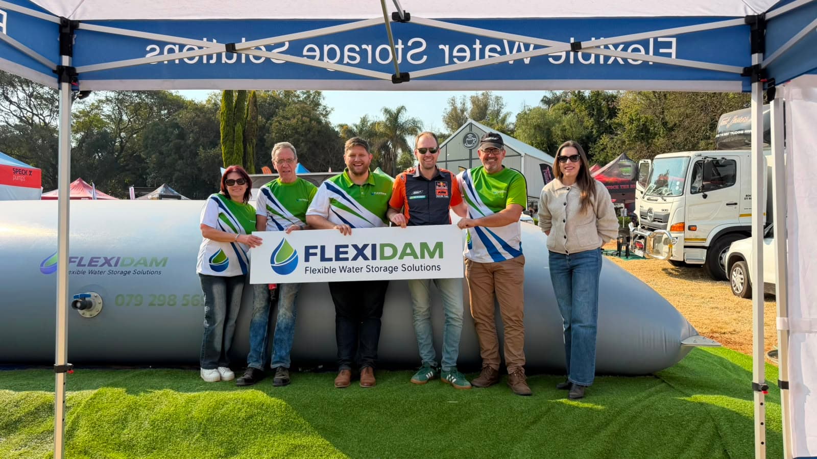 The FlexiDam team on the stand at KragDag 2026, holding a FlexiDam sign in front of a filled pillow tank